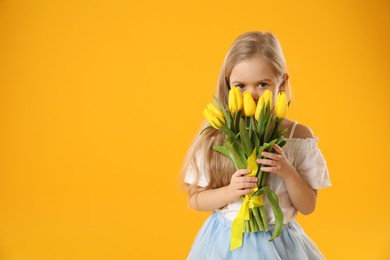 Cute little girl with beautiful yellow tulips on orange background, space for text. Spring season