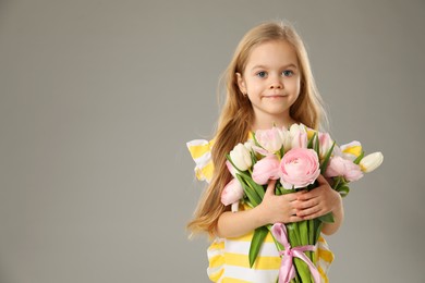 Photo of Cute little girl with bouquet of beautiful spring flowers on gray background, space for text