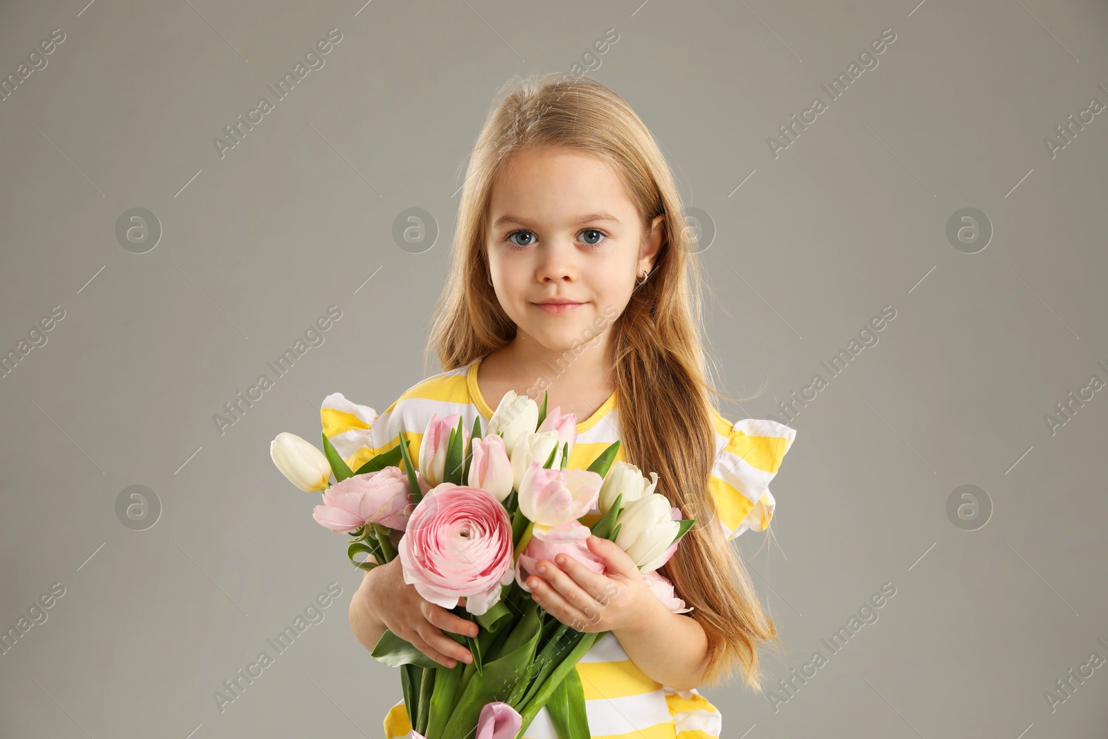 Photo of Cute little girl with bouquet of beautiful spring flowers on gray background