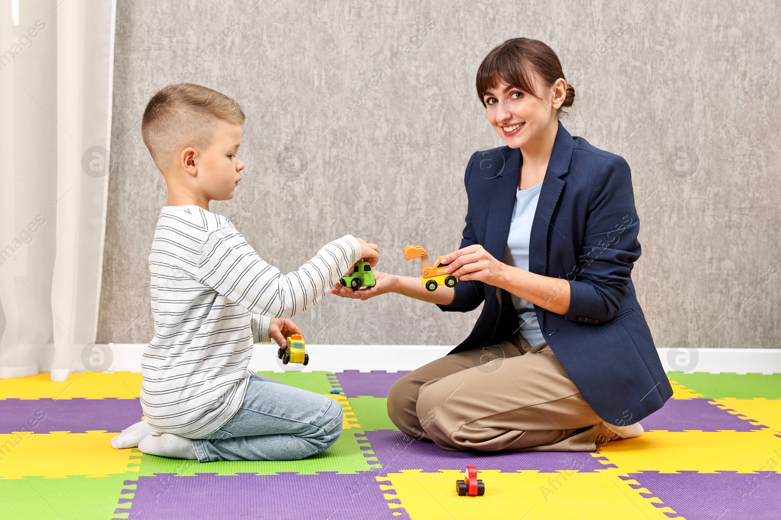 Photo of Autism therapy. Smiling psychologist and little boy playing with toy cars in mental health center