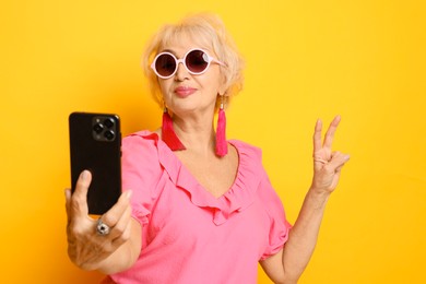 Photo of Cool grandmother showing V-sign while taking selfie on orange background