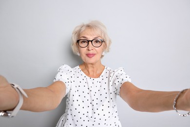 Photo of Elegant grandmother taking selfie on light grey background