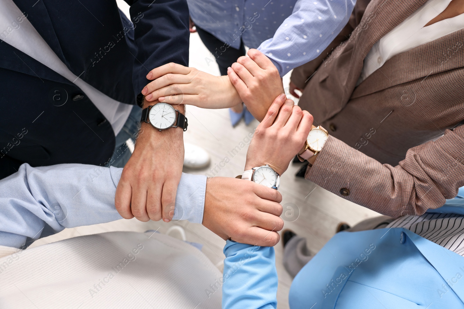 Photo of Teamwork. Group of people holding hands together indoors, top view