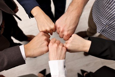 Photo of Teamwork. Group of people joining fists together indoors, top view