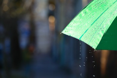 Photo of Open green umbrella under pouring rain outdoors, closeup. Space for text