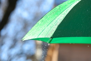 Photo of Open green umbrella under pouring rain outdoors, closeup