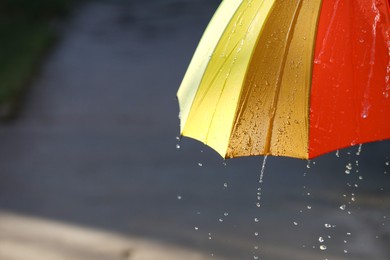 Photo of Open bright umbrella under pouring rain outdoors, closeup. Space for text