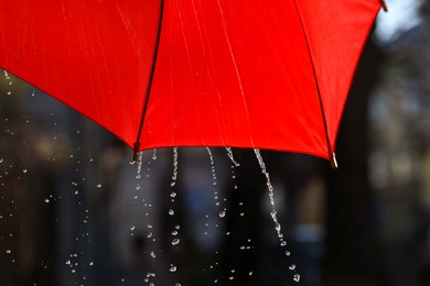 Photo of Open red umbrella under pouring rain outdoors, closeup