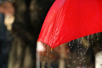 Photo of Open red umbrella under pouring rain outdoors, closeup