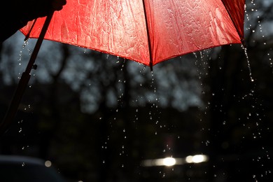 Photo of Open red umbrella under pouring rain outdoors, closeup