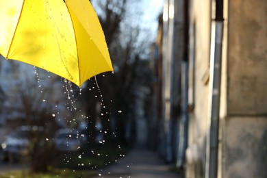 Photo of Open yellow umbrella under pouring rain outdoors, closeup. Space for text