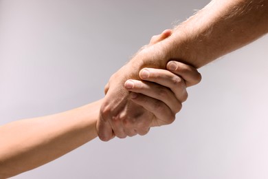 Photo of Help and support. People holding hands on light grey background, closeup