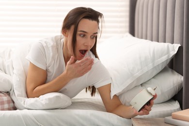 Overslept woman with alarm clock in bed at home