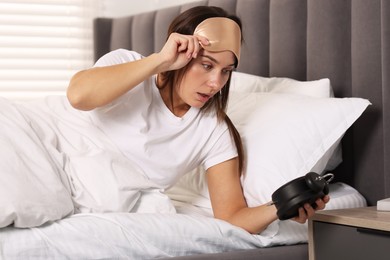 Overslept woman with alarm clock in bed at home