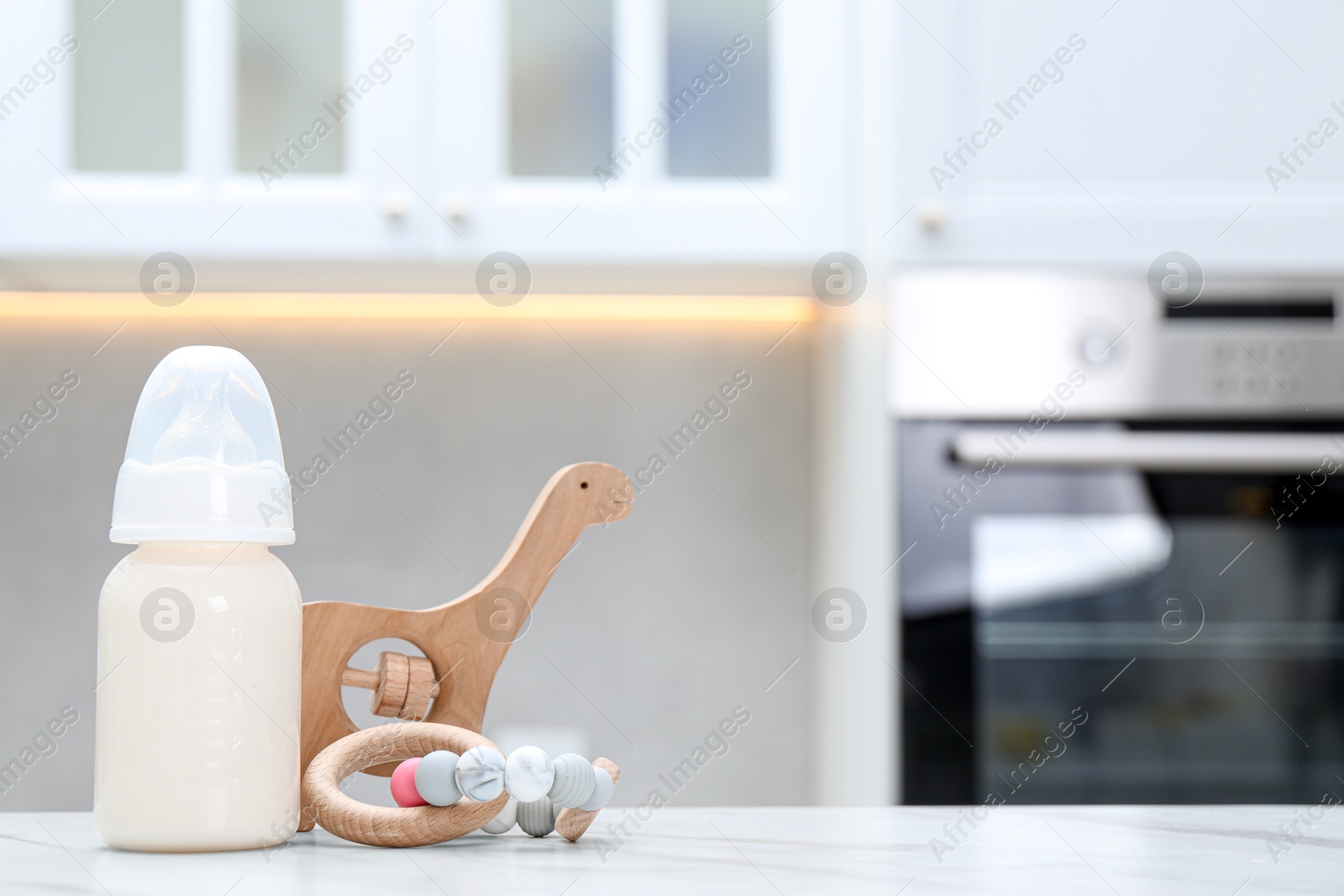 Photo of Feeding bottle with milk and toys on white table indoors. Space for text