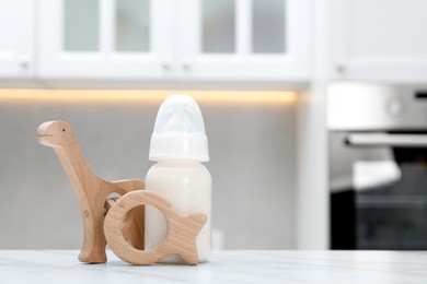 Photo of Feeding bottle with milk and toys on white table indoors. Space for text