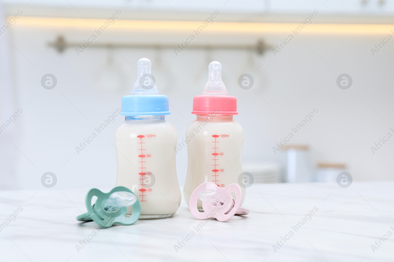 Photo of Feeding bottles with baby formula and pacifiers on white table indoors