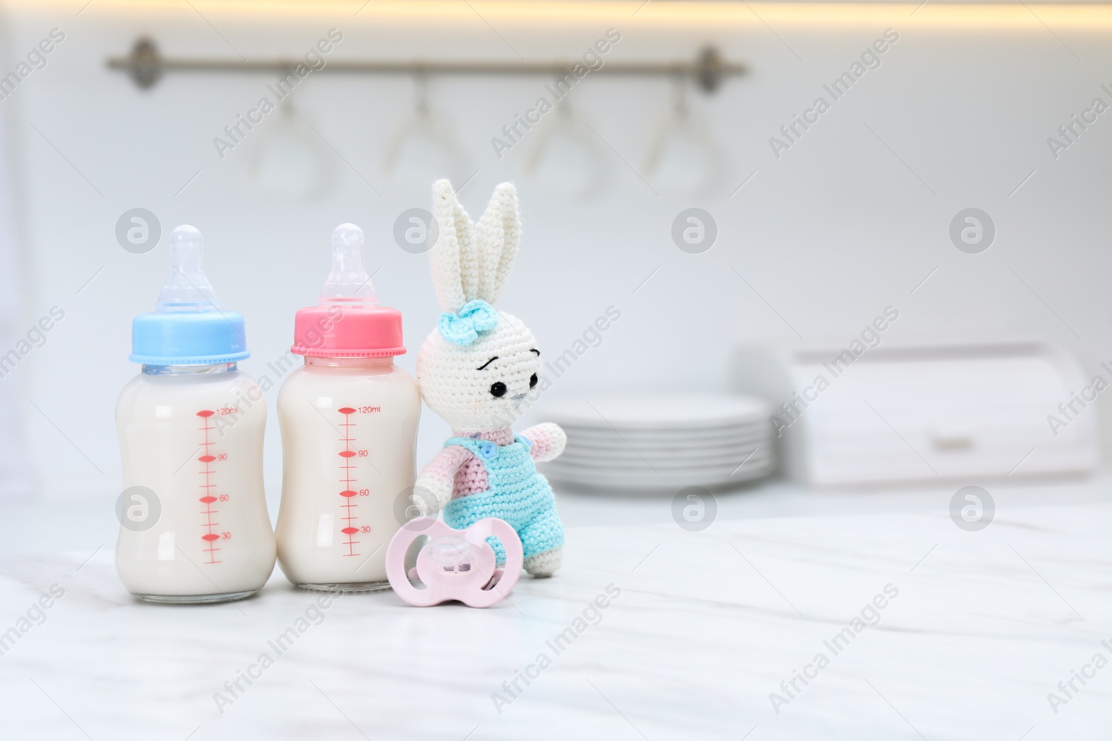 Photo of Feeding bottles with baby formula, pacifier and toy bunny on white table indoors. Space for text