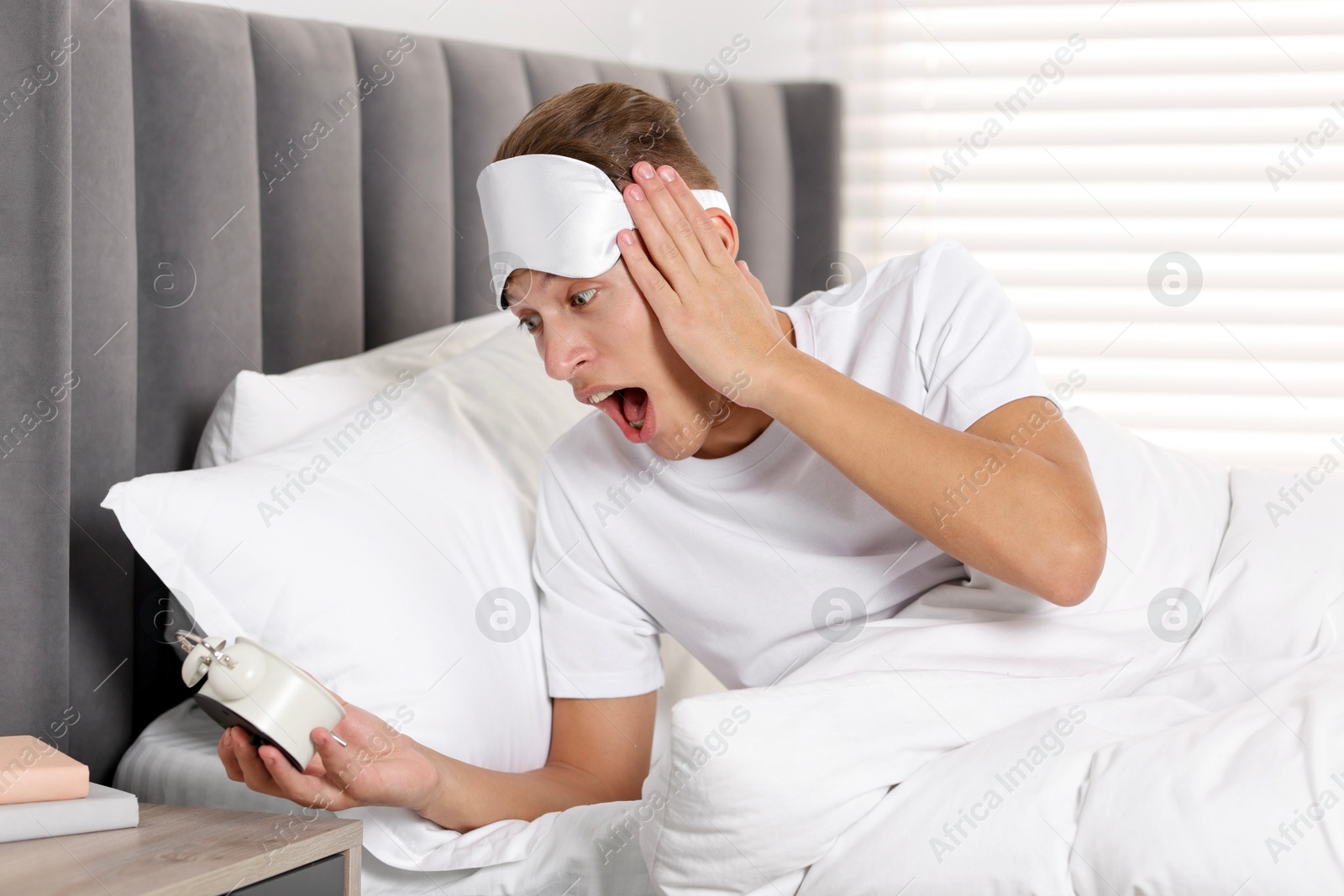 Photo of Overslept man with alarm clock in bed at home