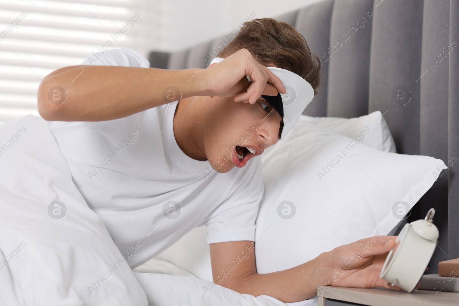 Photo of Overslept man with alarm clock in bed at home