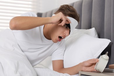 Photo of Overslept man with alarm clock in bed at home