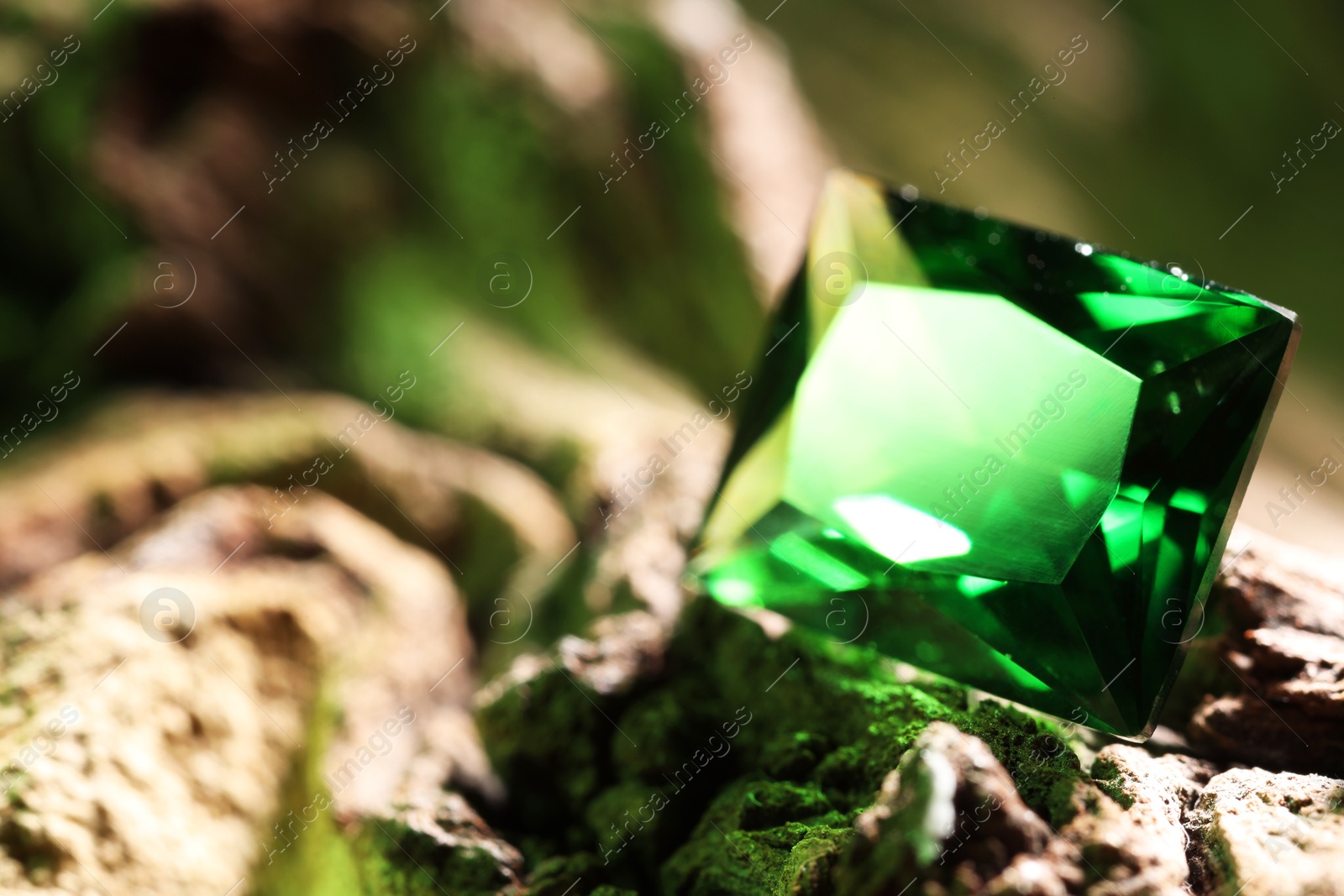 Photo of Beautiful shiny green gemstone on stone, closeup. Space for text