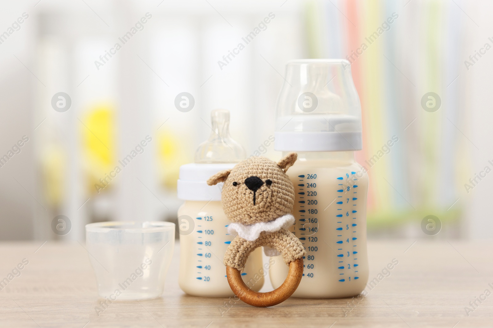 Photo of Feeding bottles with milk and rattle on wooden table indoors