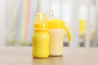 Photo of Feeding bottles with milk on wooden table indoors