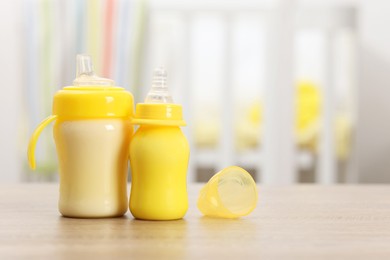 Photo of Feeding bottles with milk on wooden table indoors