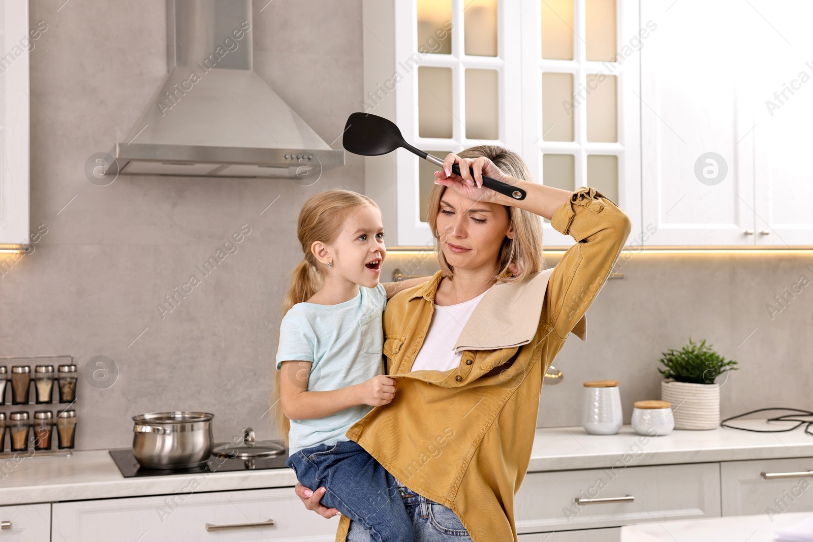 Photo of Tired housewife holding her daughter while cooking in kitchen