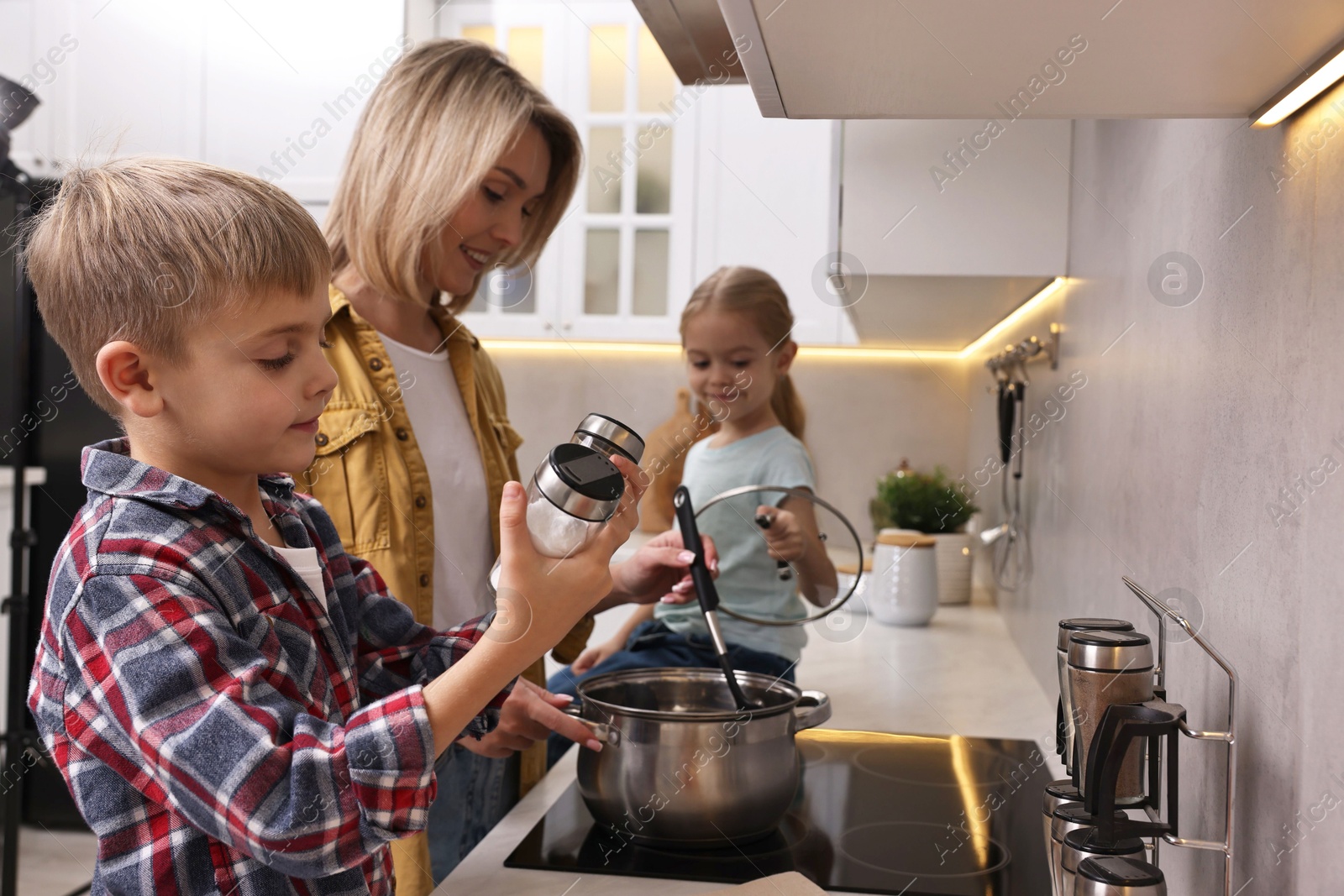 Photo of Happy housewife and her kids cooking together on stove in kitchen