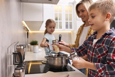 Happy housewife and her kids cooking together on stove in kitchen