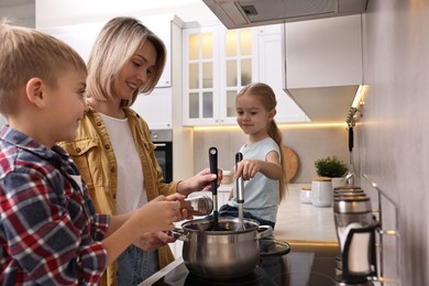 Happy housewife and her kids cooking together on stove in kitchen