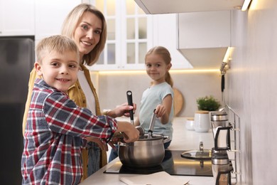 Photo of Happy housewife and her kids cooking together on stove in kitchen