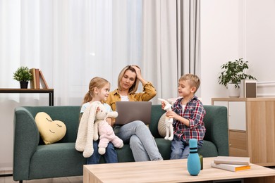 Photo of Tired housewife using laptop while her kids playing with toys at home