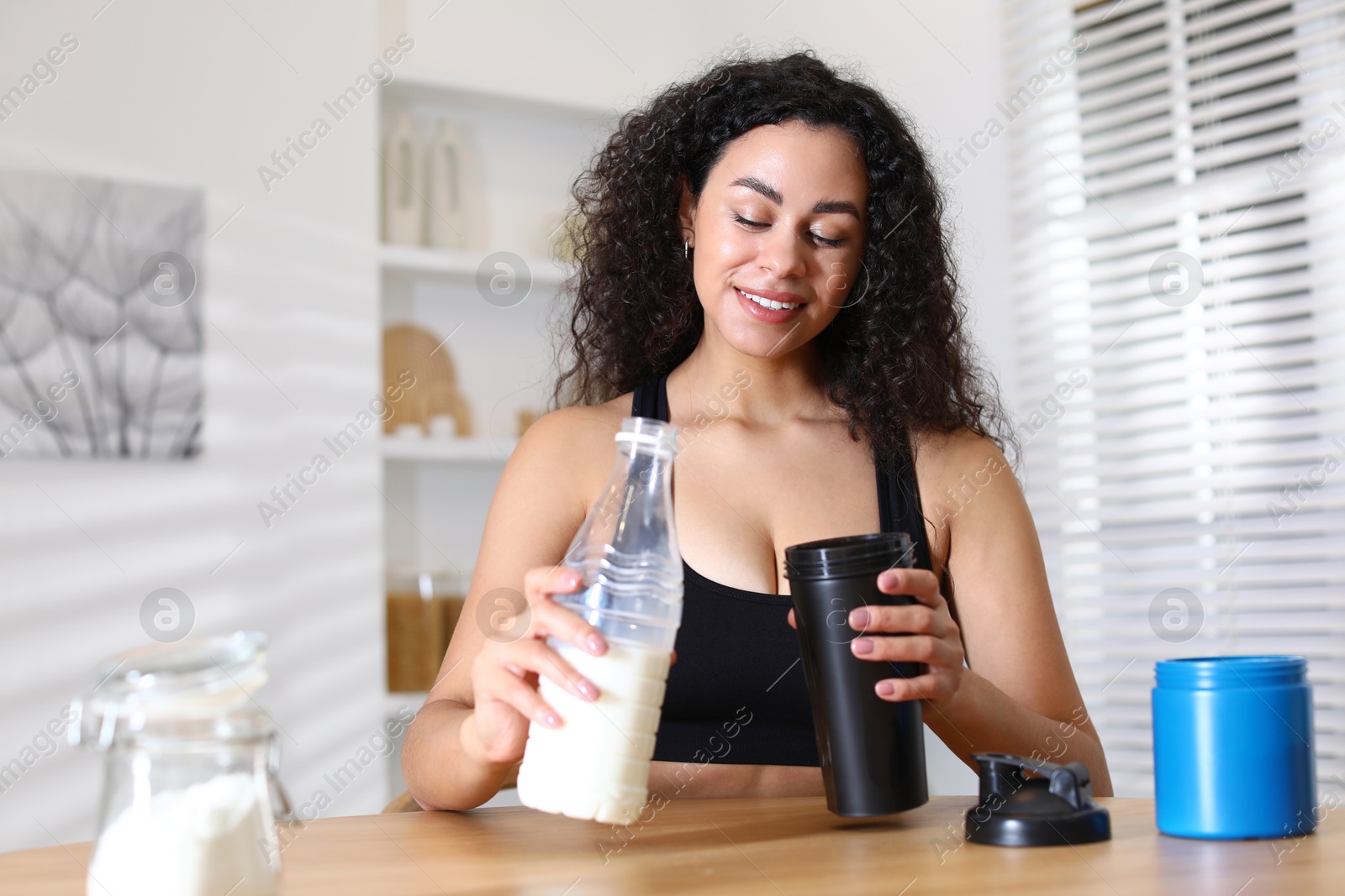 Photo of Beautiful woman making protein shake at wooden table indoors