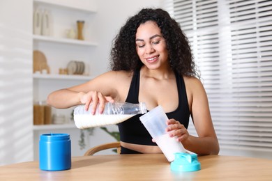 Photo of Beautiful woman making protein shake at wooden table indoors