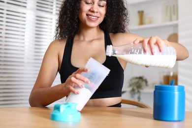 Photo of Beautiful woman making protein shake at wooden table indoors, closeup