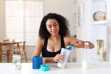 Photo of Beautiful woman making protein shake at white table indoors