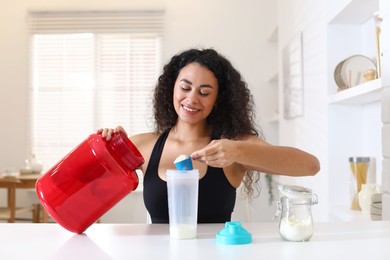 Photo of Beautiful woman making protein shake at white table indoors