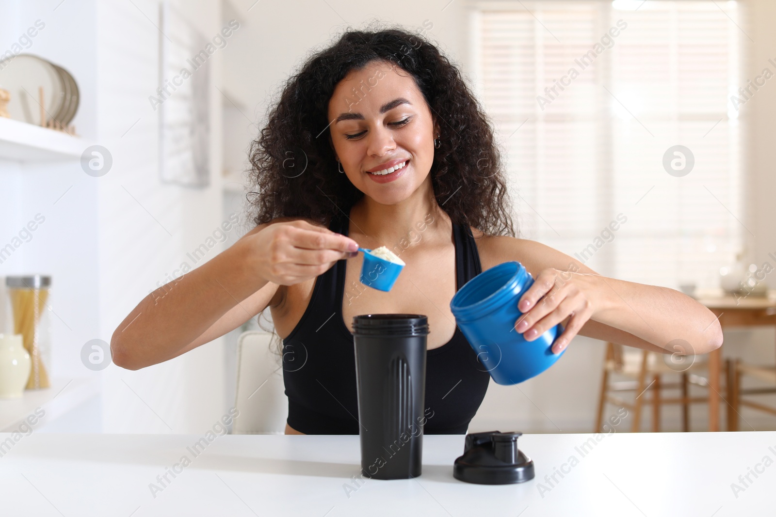 Photo of Beautiful woman making protein shake at white table indoors