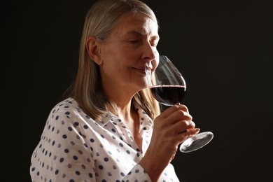 Photo of Professional sommelier tasting red wine in glass on black background