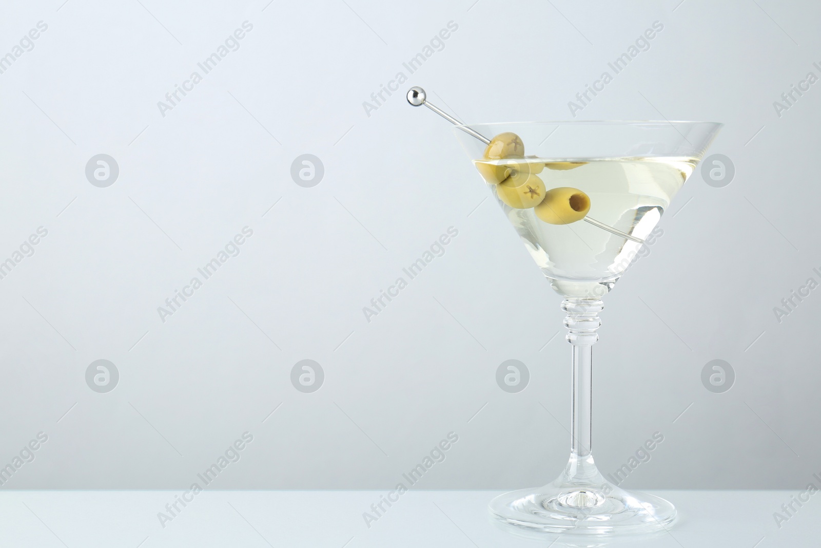 Photo of Martini cocktail with olives in glass on light table, space for text