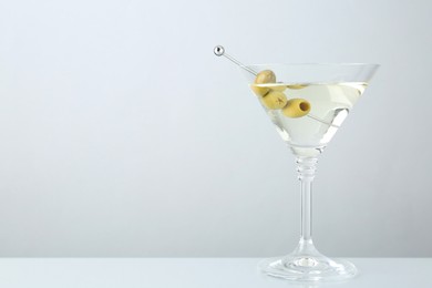 Photo of Martini cocktail with olives in glass on light table, space for text