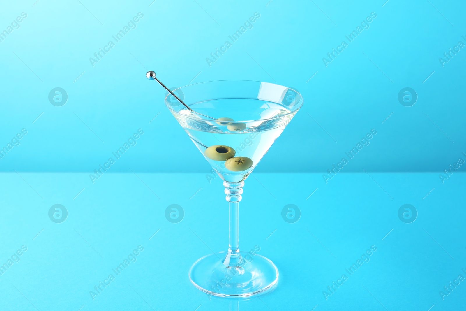 Photo of Martini cocktail with olives in glass on light blue background