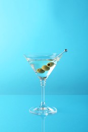 Photo of Martini cocktail with olives in glass on light blue background