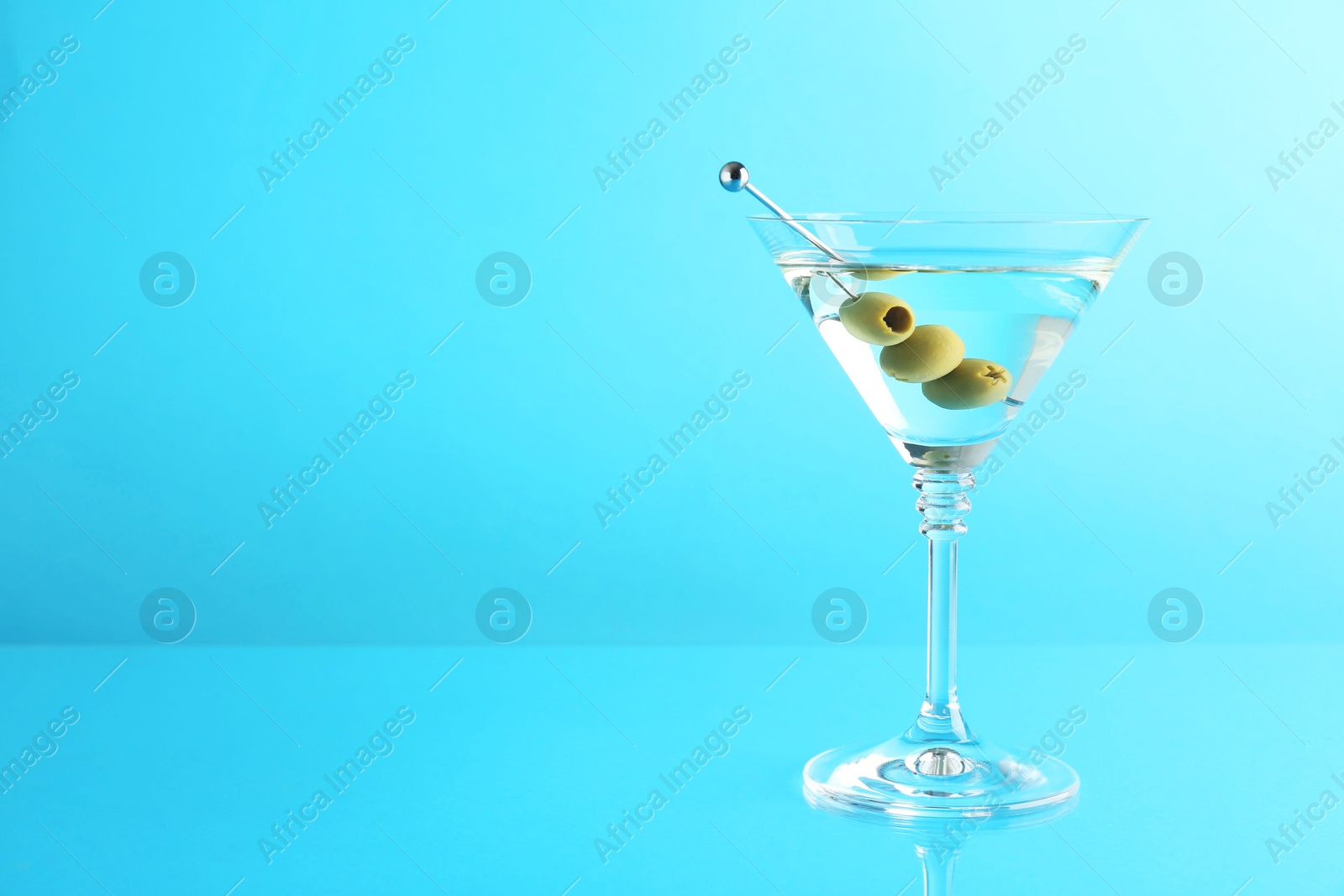 Photo of Martini cocktail with olives in glass on light blue background, space for text