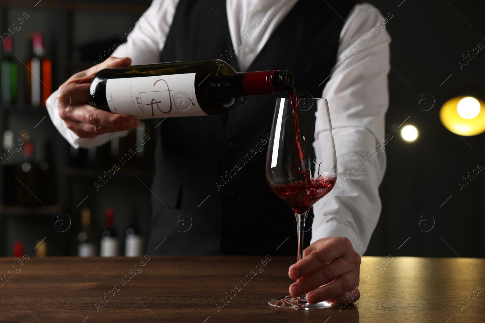 Photo of Professional sommelier pouring red wine into glass at wooden table indoors, closeup