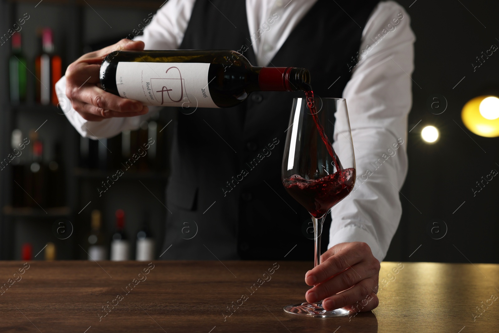 Photo of Professional sommelier pouring red wine into glass at wooden table indoors, closeup