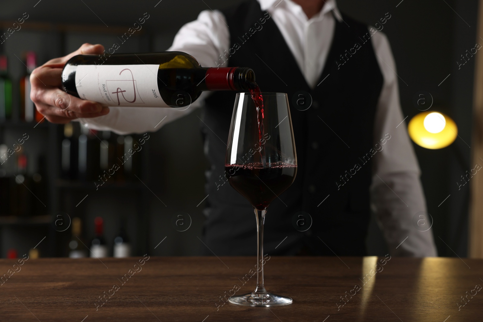 Photo of Professional sommelier pouring red wine into glass at wooden table indoors, closeup